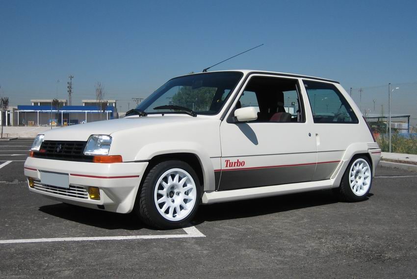 Coche compacto blanco con detalles en rojo y llantas blancas, estacionado en un área urbana.