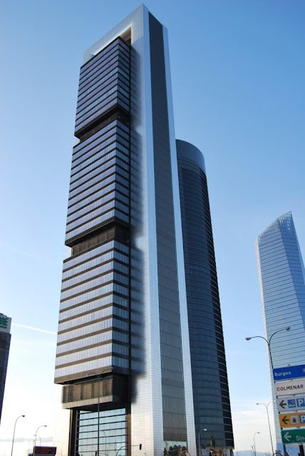 Rascacielos moderno con fachada de vidrio y estructuras horizontales en un entorno urbano.