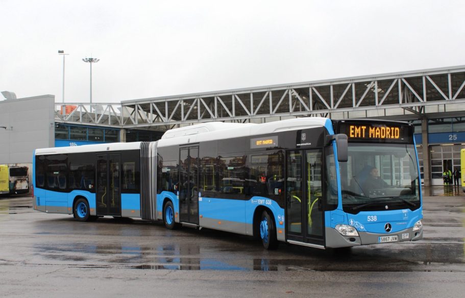 Autobús articulado azul y blanco estacionado en una terminal, con destino visible.