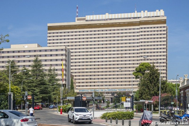 Edificio moderno con cartel en la parte superior y árboles alrededor, en un día soleado.