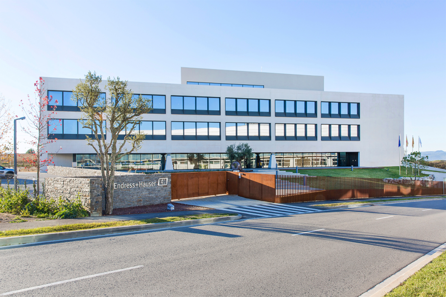 Edificio moderno de tres plantas con fachada blanca y amplios ventanales.