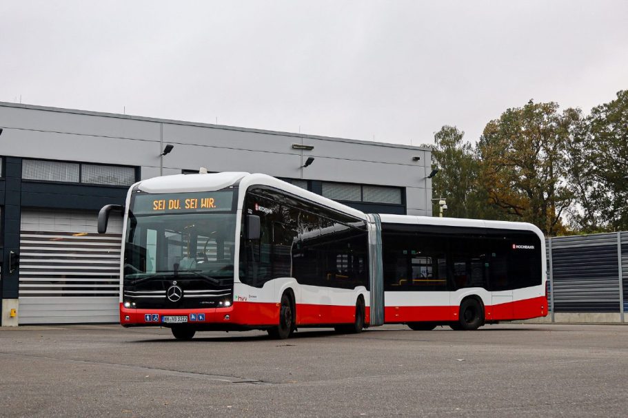 Autobús articulado rojo y blanco estacionado frente a un taller.