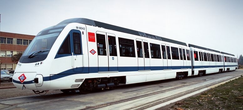 Tren CAF serie 8000 Metro de Madrid Tren moderno de metro blanco y azul en una vía, rodeado de edificios.