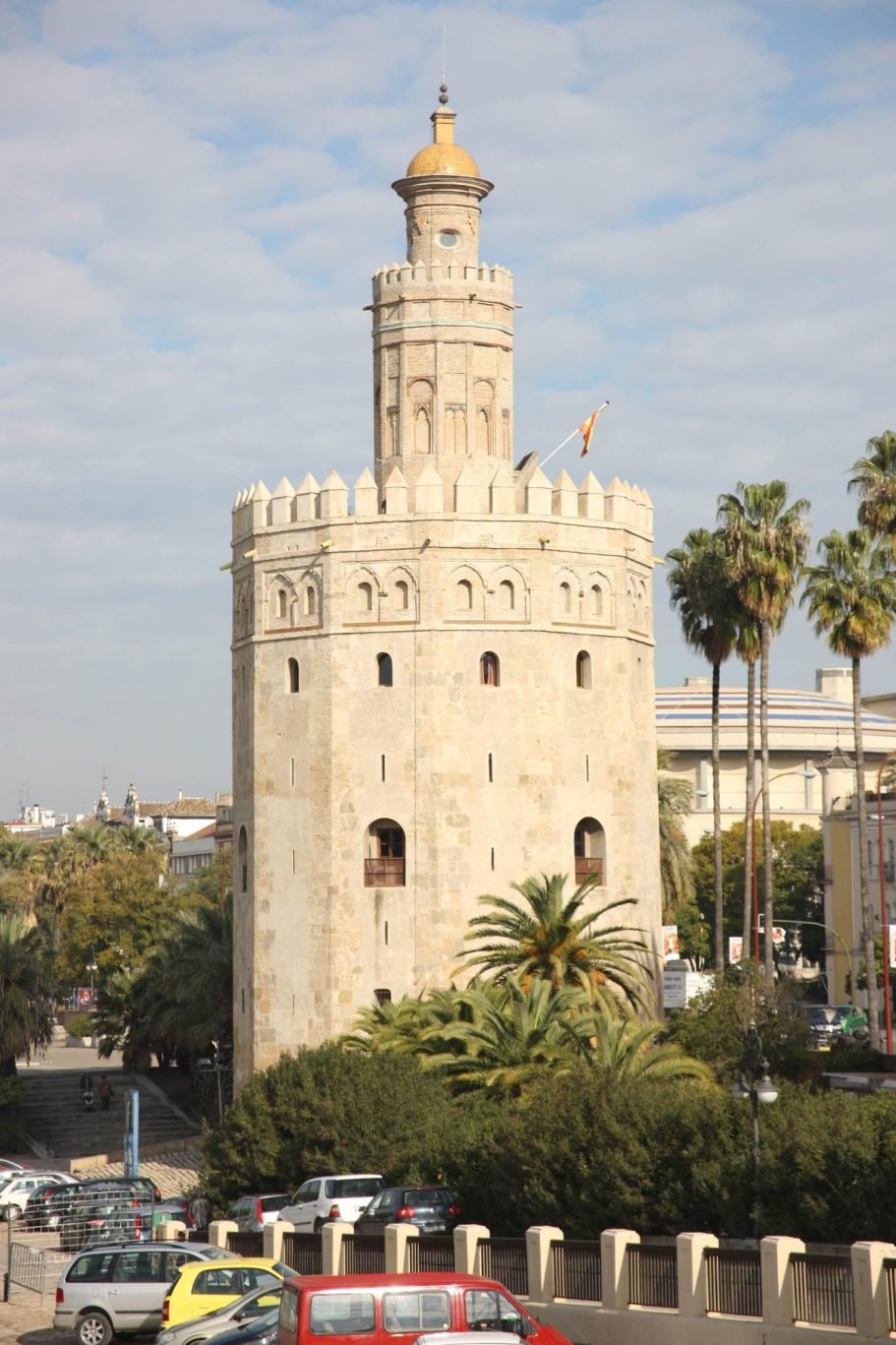 Torre histórica de Sevilla, con palmeras y cielo nublado de fondo.