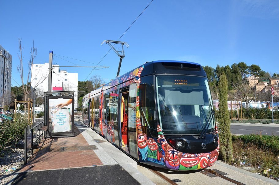 Tranvía Alstom Citadis Compact Tranvía colorido en una parada con un paisaje urbano al fondo.